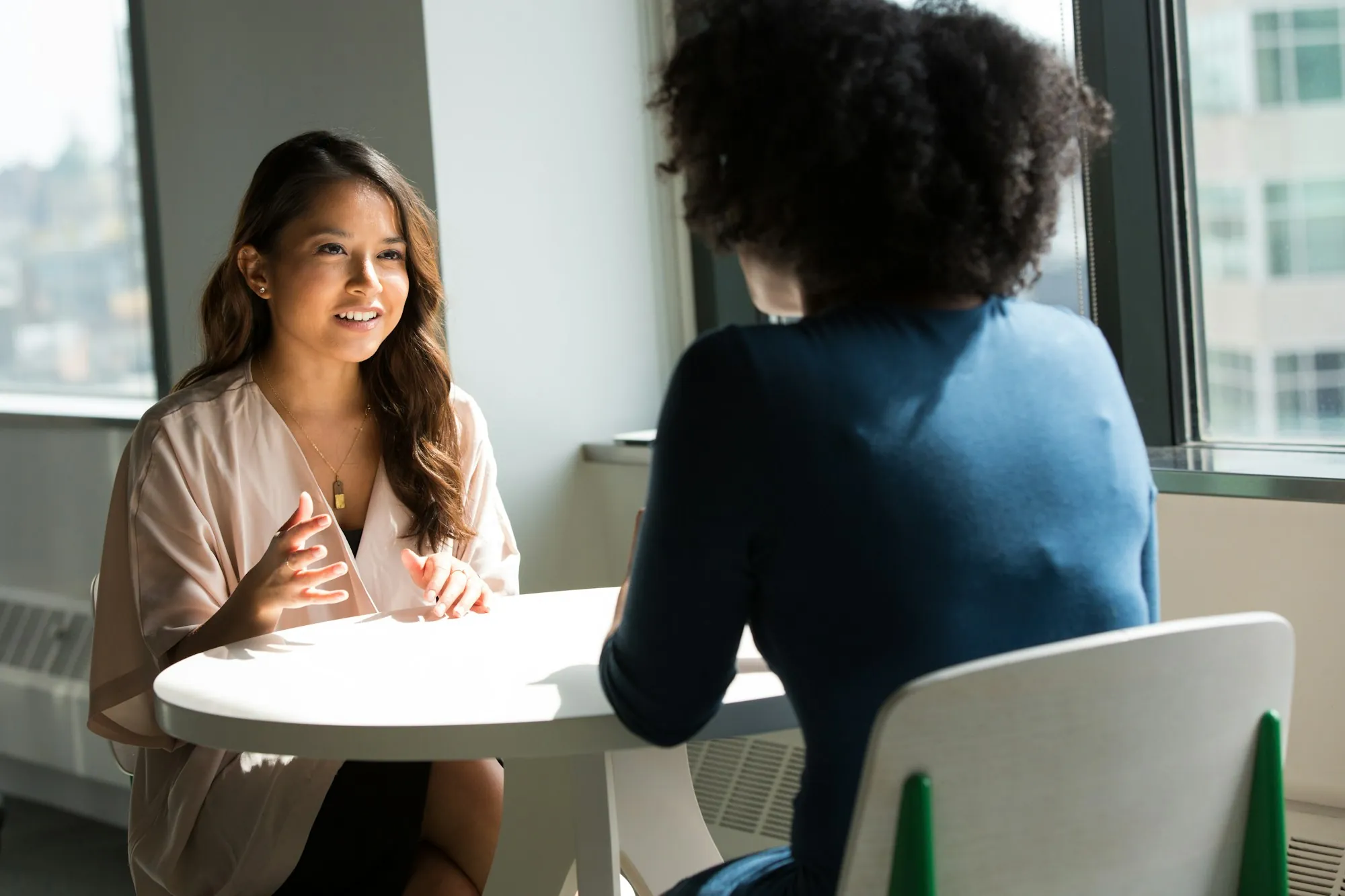 Two people sitting and talking across a small table in a bright room