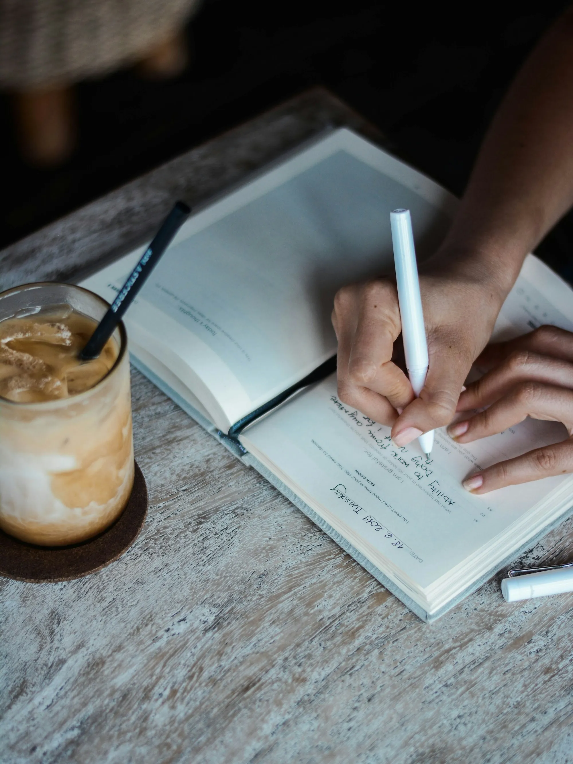 A person writing in an open notebook on a wooden table
