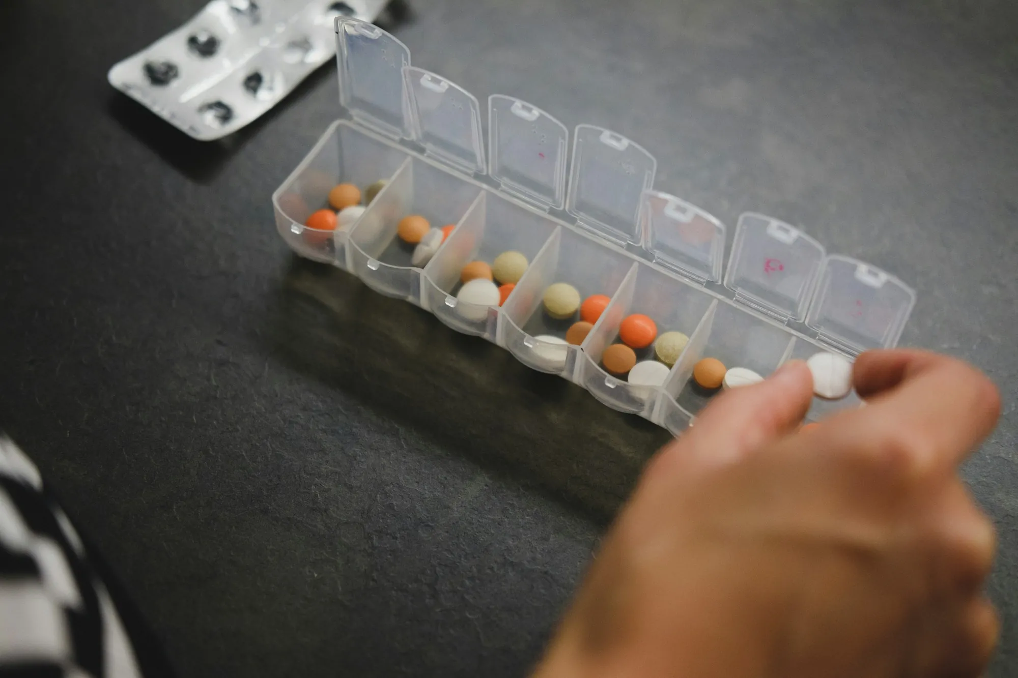 A hand filling a weekly pill organiser on a table